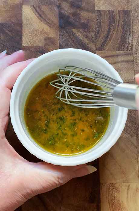 Whisking the melted butter with the seasonings in a small, white ramekin.