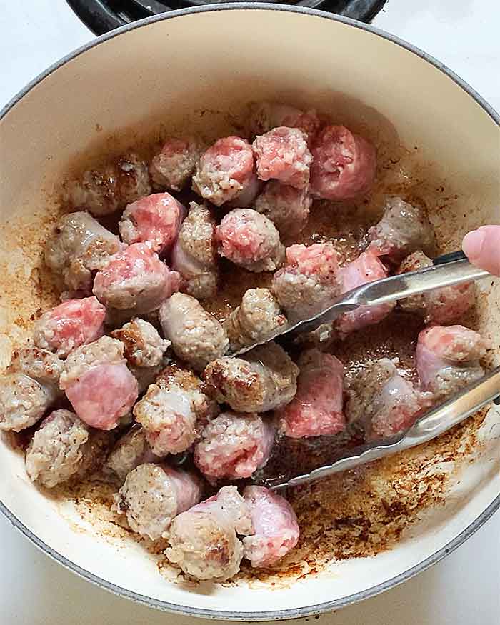 Cooking the sausage pieces in the bacon drippings to brown the sides.