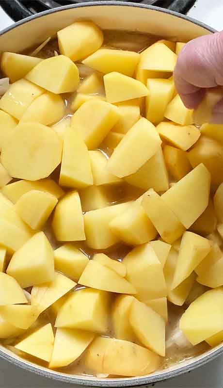 Layering chunks of gold potatoes on top of the stew before placing in the oven.