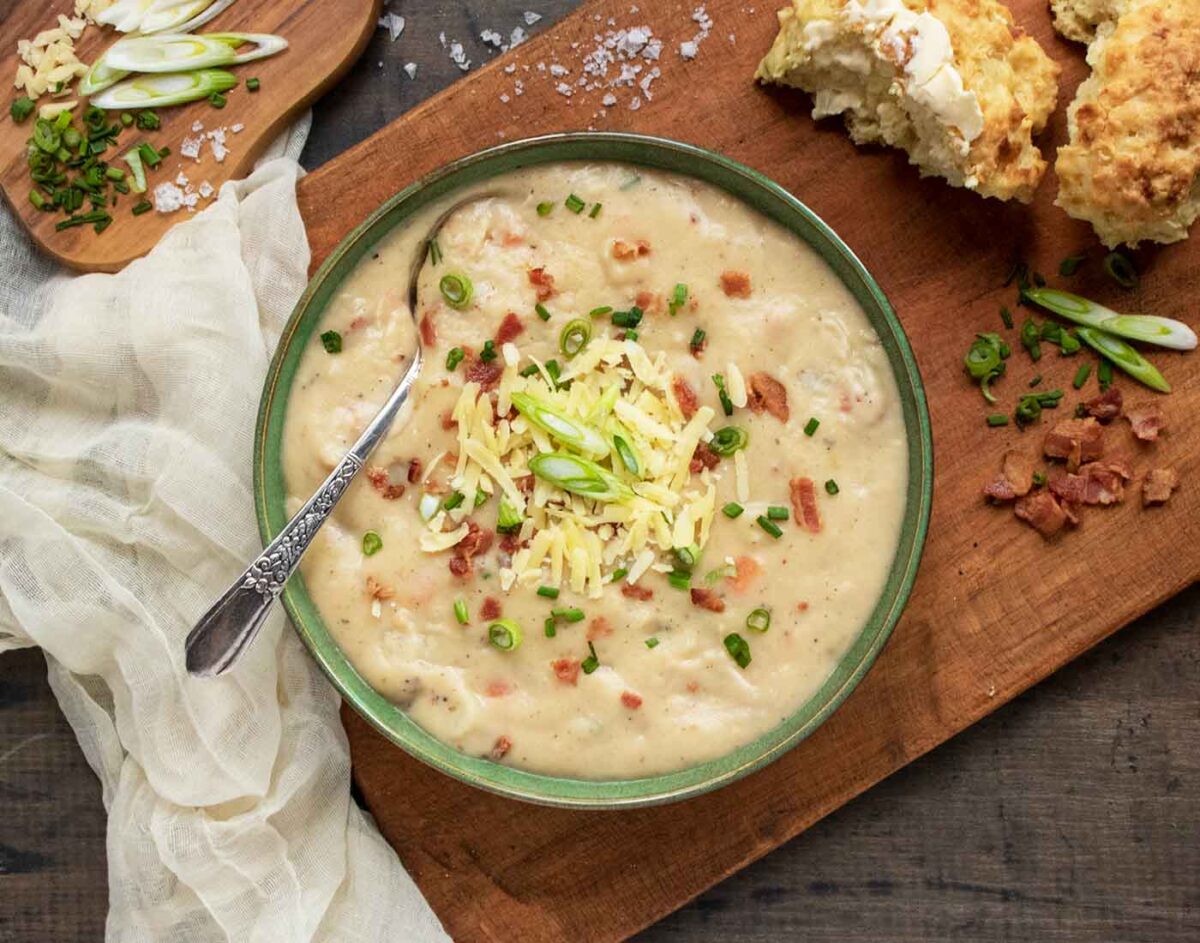 Overhead view of a bowl of Irish Potato Soup on a wooden serving board.