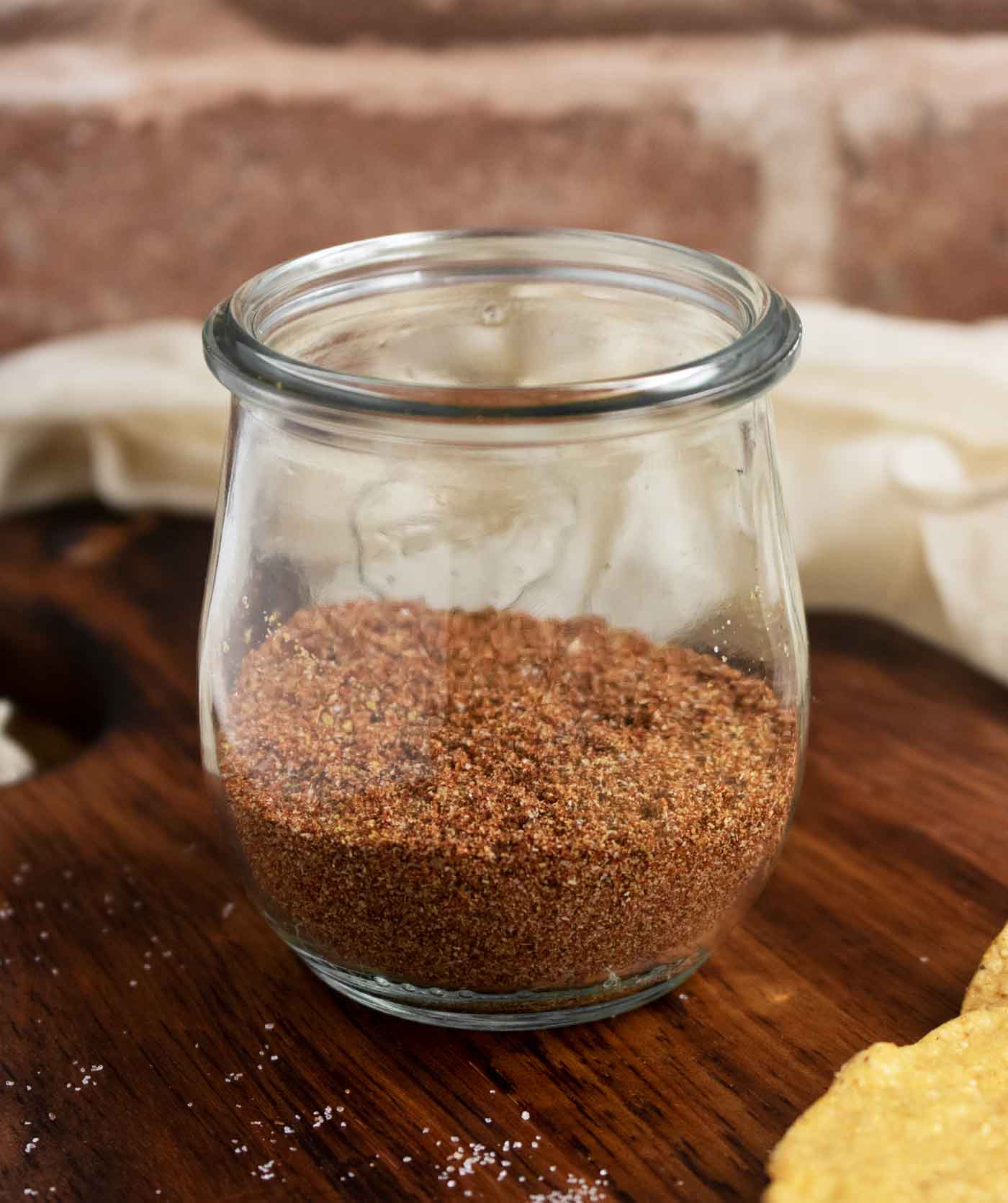 Side view of a Weck jar half-filled with taco seasoning, on a wooden serving board.