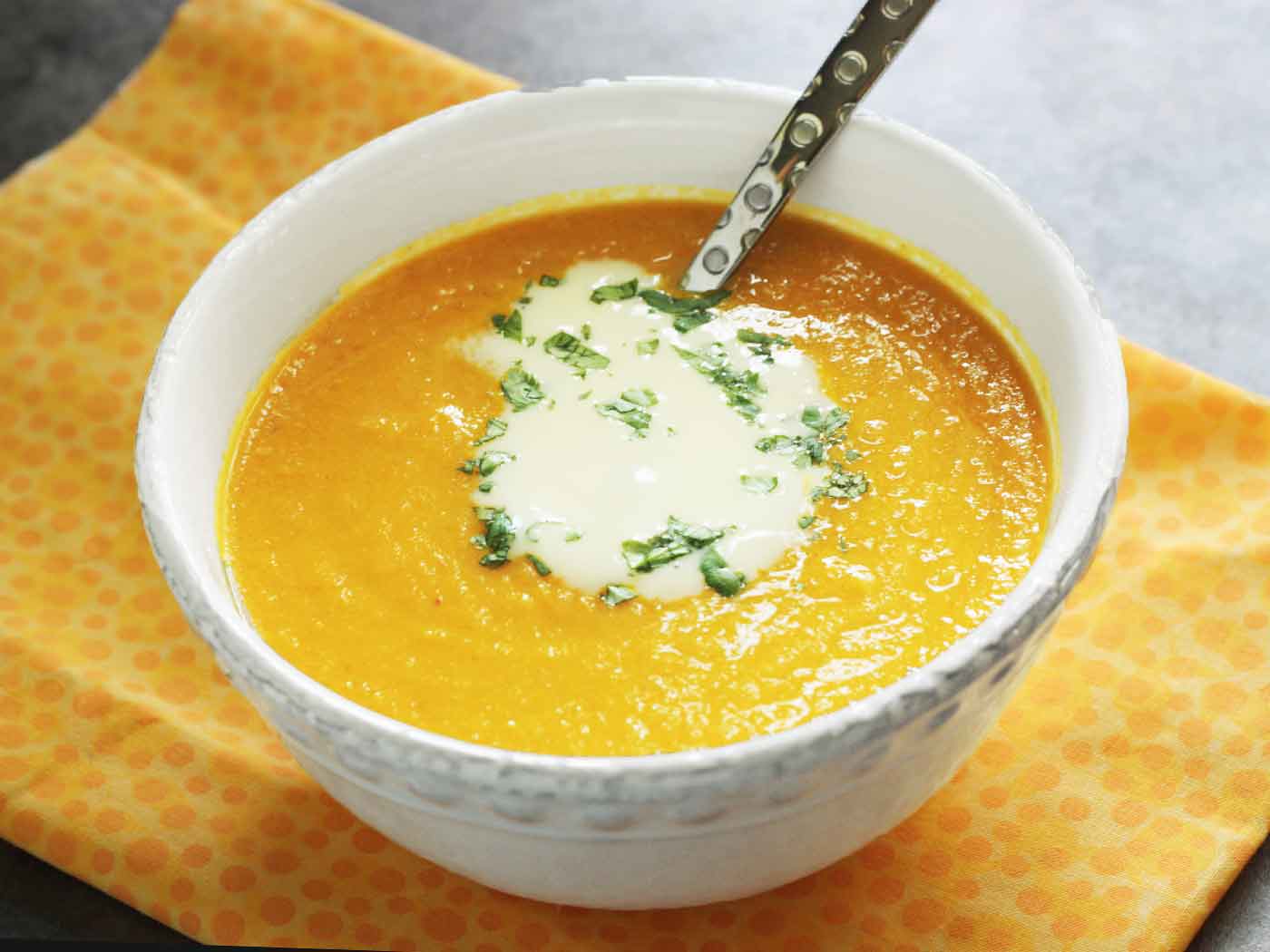 Side view of a bowl of Carrot Ginger Soup with a spoon.