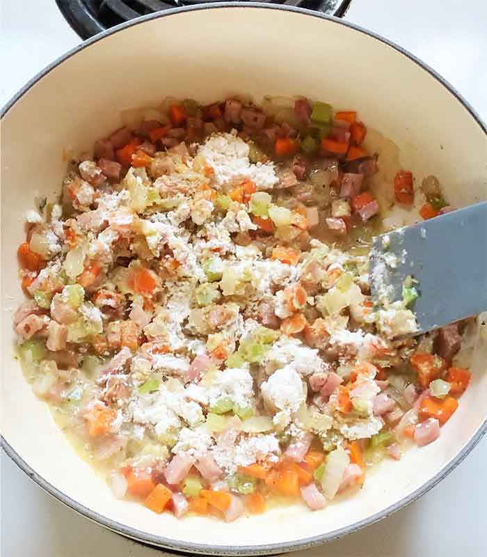 Stirring flour into the mixture that will later thicken the soup.