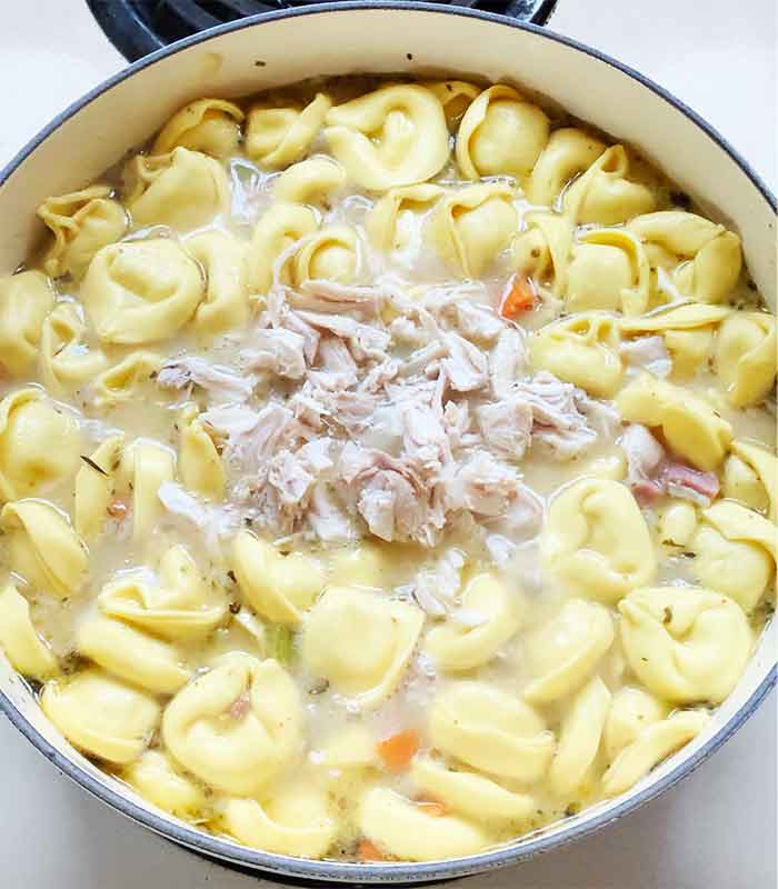 Adding the shredded rotisserie chicken to the soup.