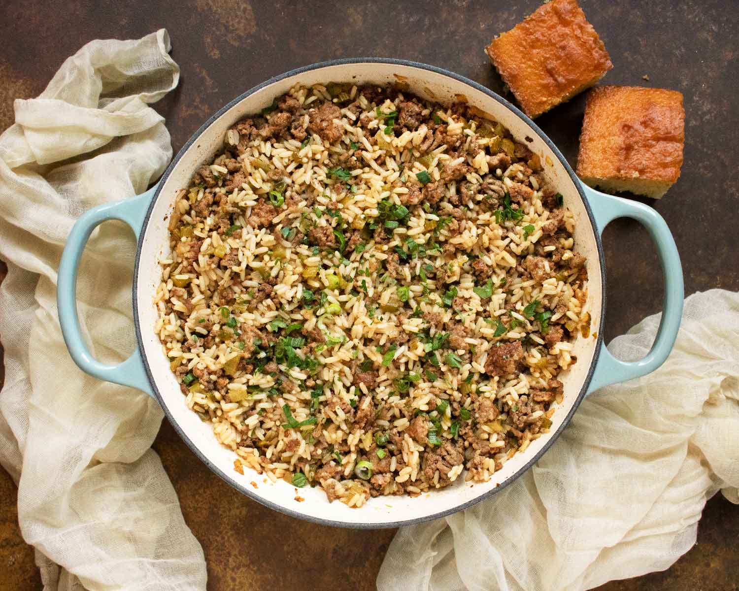 Overhead view of a skillet of Easy Dirty Rice, with a side of two pieces of cornbread.