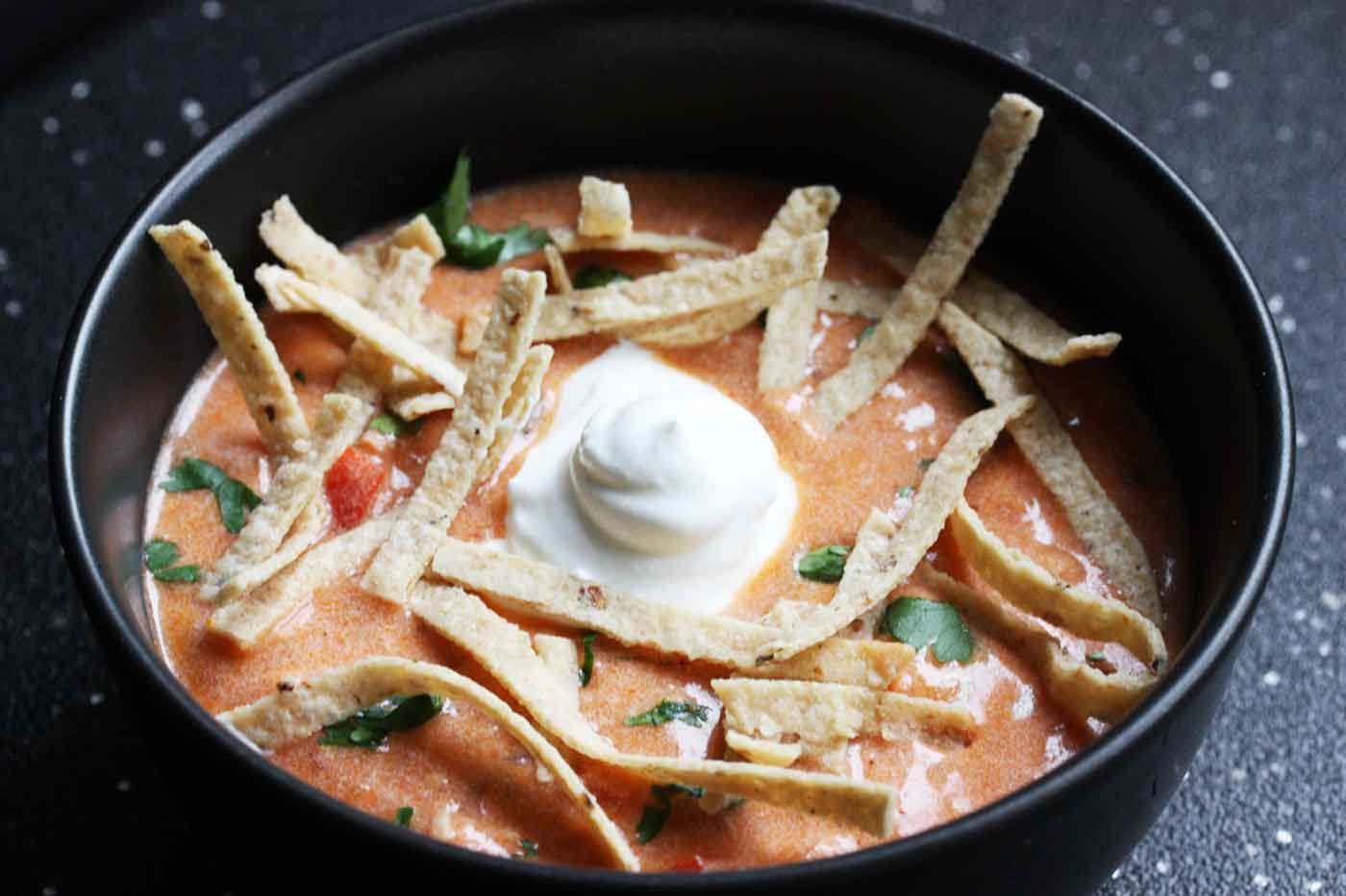 Side angled view of Chicken Tortilla Soup in a black bowl.