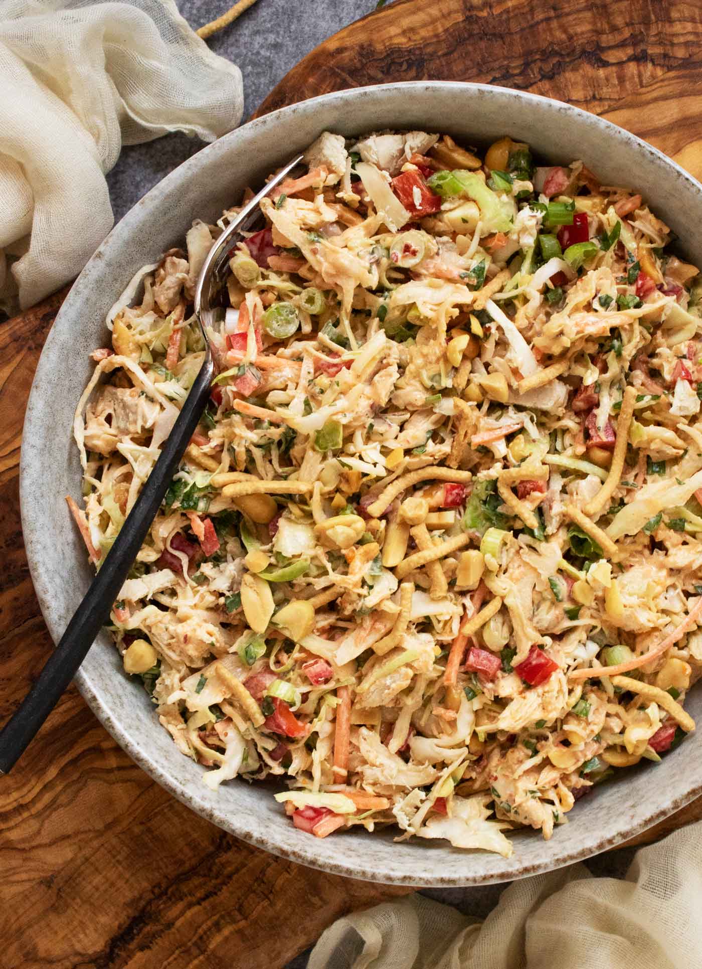 Overhead view of a bowl of Chili Crisp Chopped Chicken Salad with a fork, on a wooden serving board.