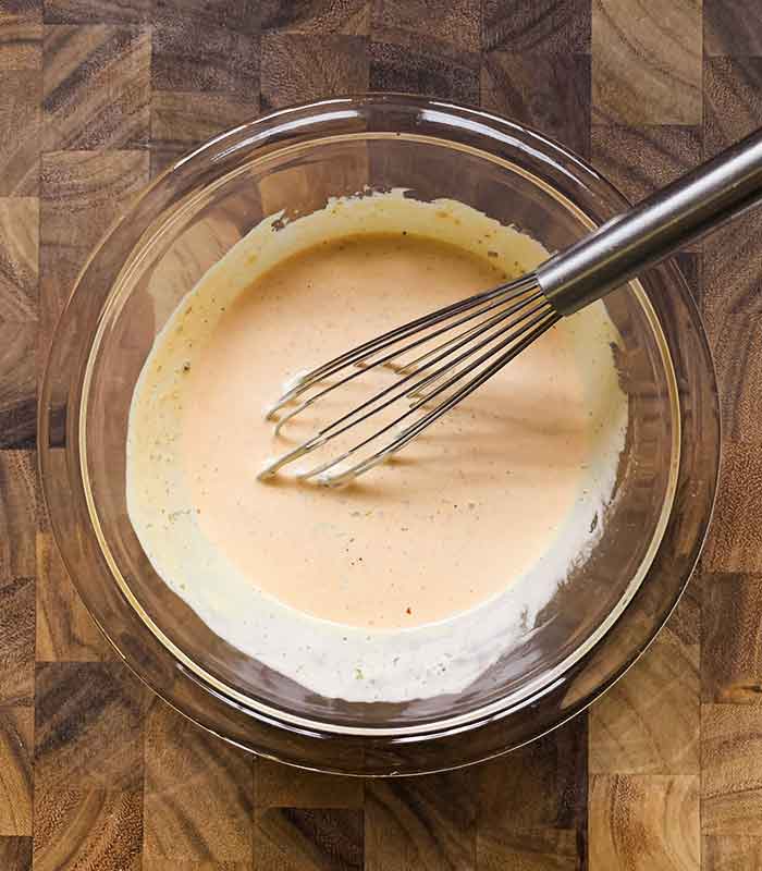 The dressing fully whisked and combined, with the whisk resting inside the glass bowl.