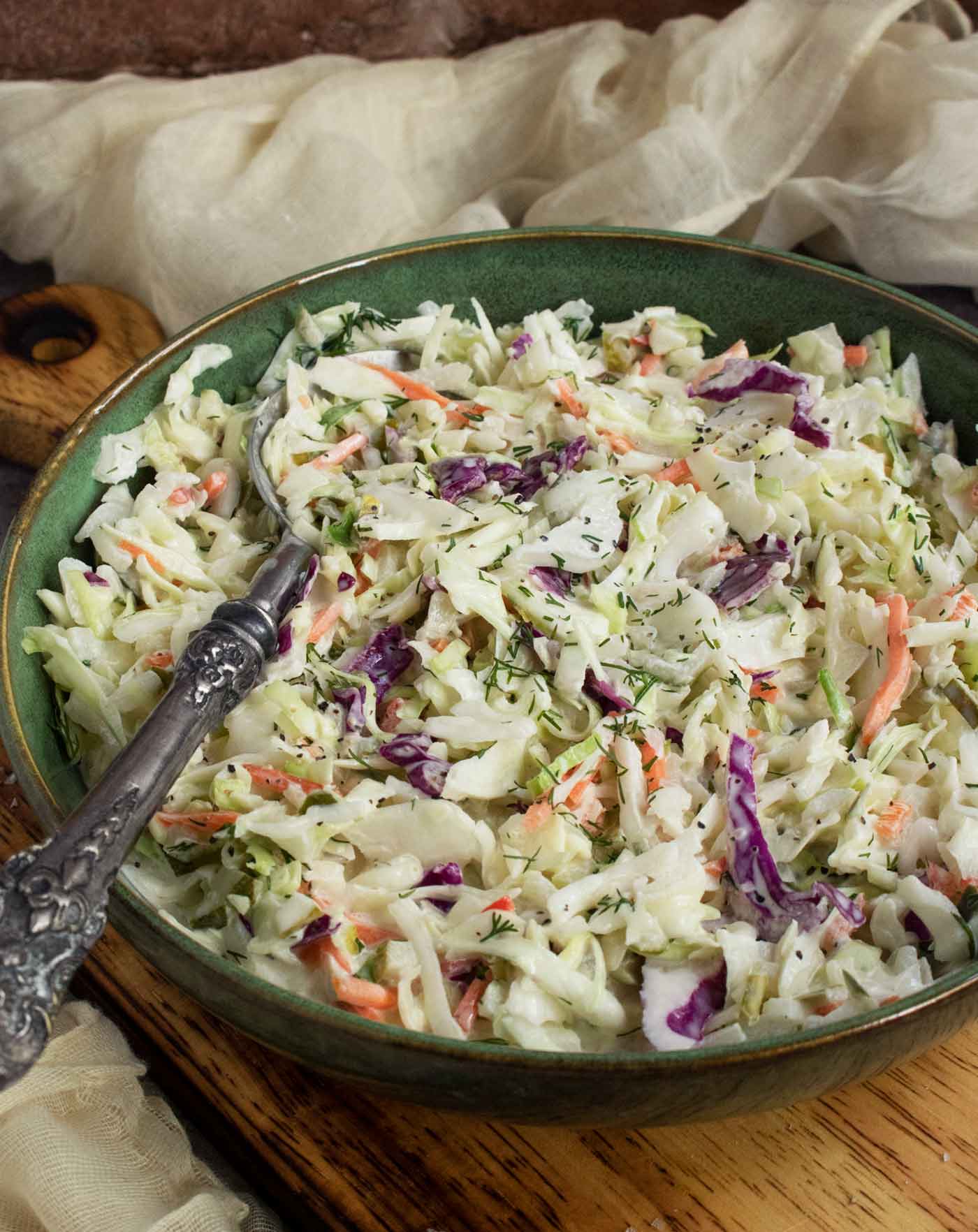 Side-angled view of the slaw in a green bowl with a serving spoon.