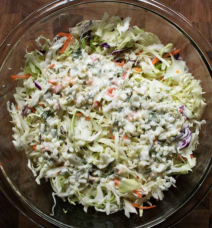 Adding dressing to the cabbage, in a large glass bowl.