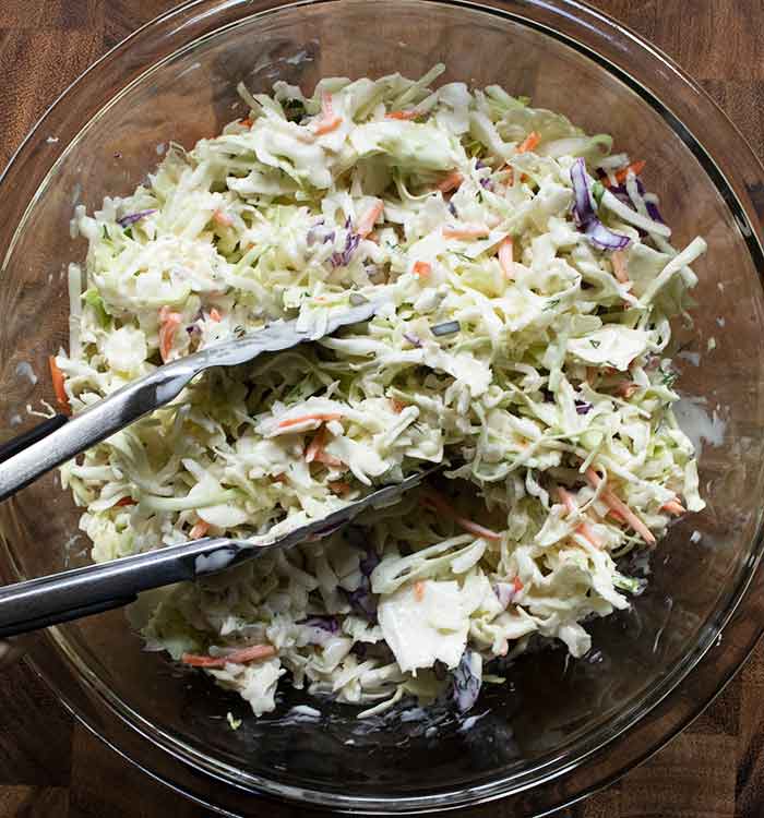 Tossing the slaw and dressing with tongs.
