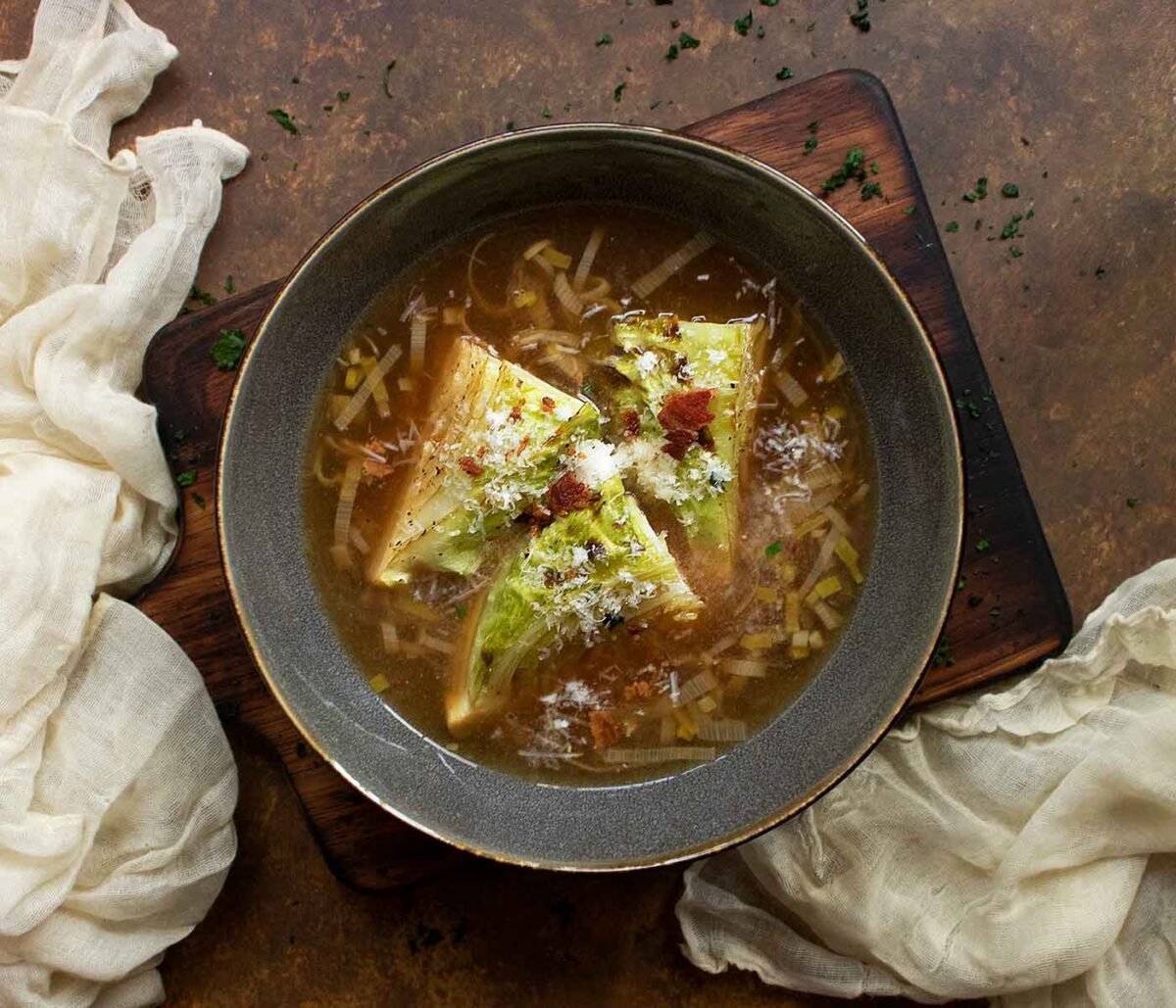 An overhead view of a Roasted Cabbage Broth Bowl, in a dark gray on a wooden serving board.