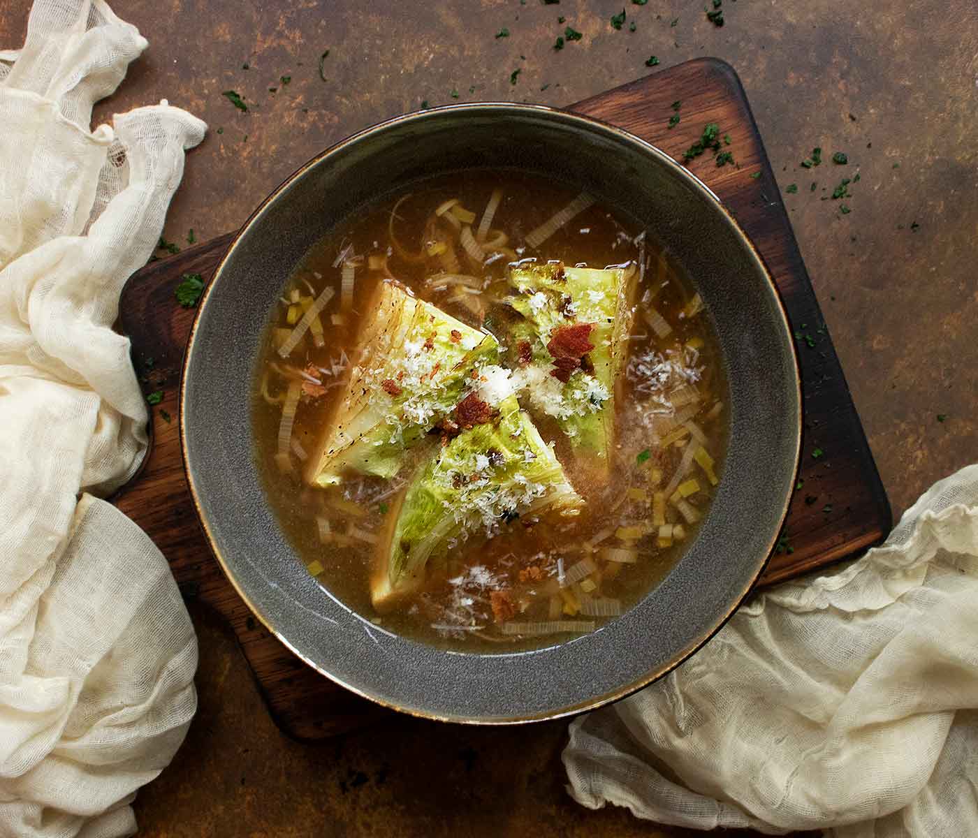 An overhead view of a Roasted Cabbage Broth Bowl, in a dark gray on a wooden serving board.