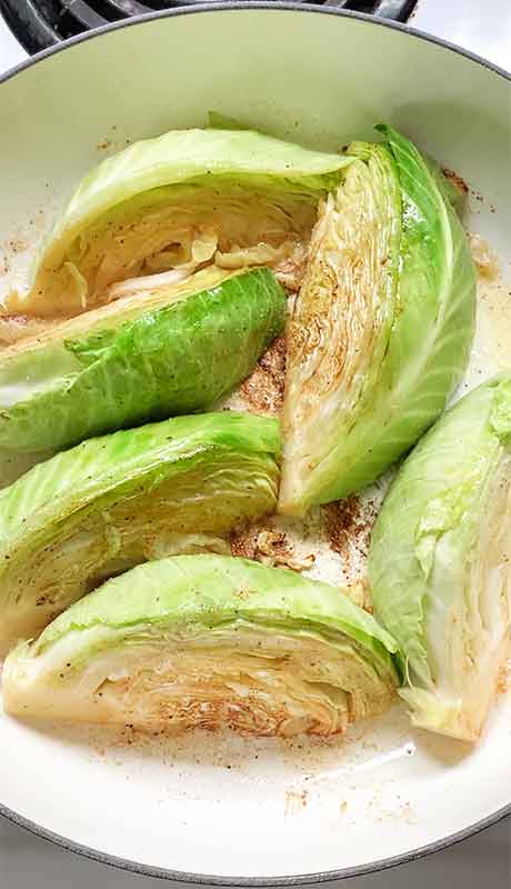 Cabbage wedges searing on the second side, with the lightly browned side facing up.