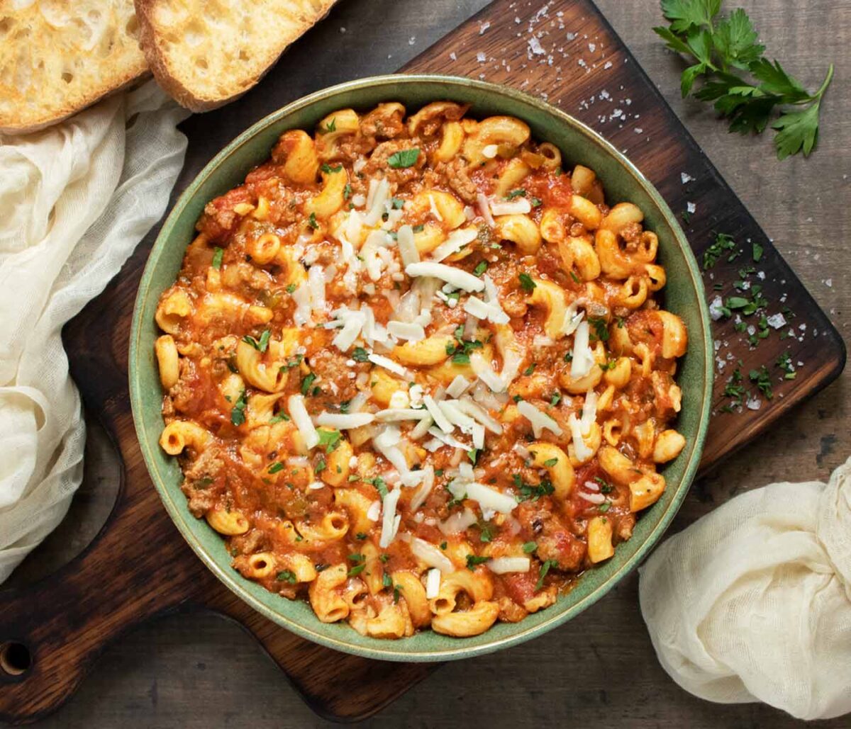 American Goulash in a green bowl on a wooden board.