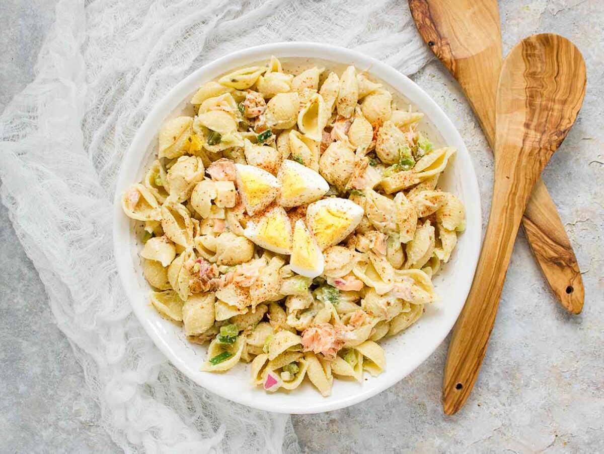 An overhead view of Smoke Salmon Pasta Salad in a white salad bowl with wooden spoons.