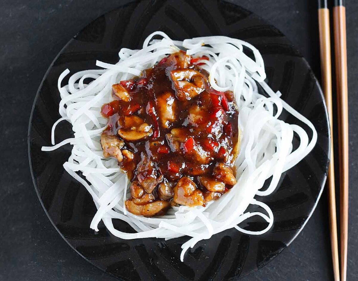 Overhead view of Thai Chicken with Rice Noodles on a black plate with chopsticks to the side.
