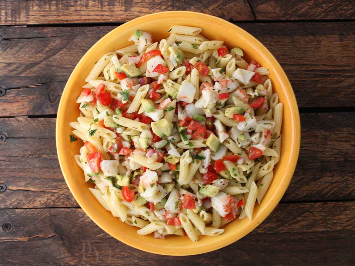 Overhead view of Avocado and Crab Pasta Salad in a bright yellow serving bowl.