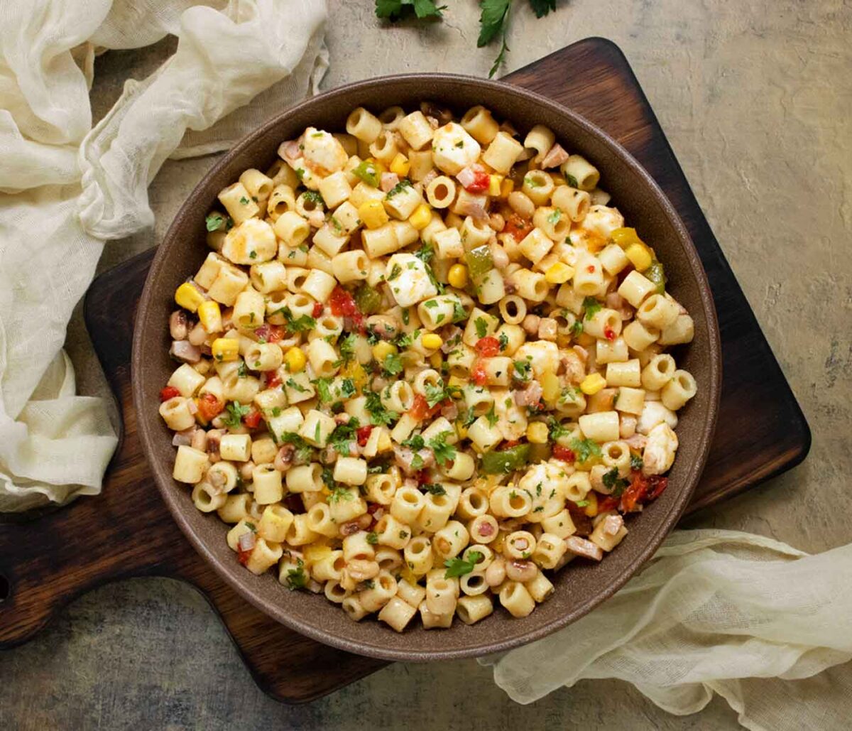 Cowboy Caviar Pasta Salad in a brick colored bowl on a wooden serving board.