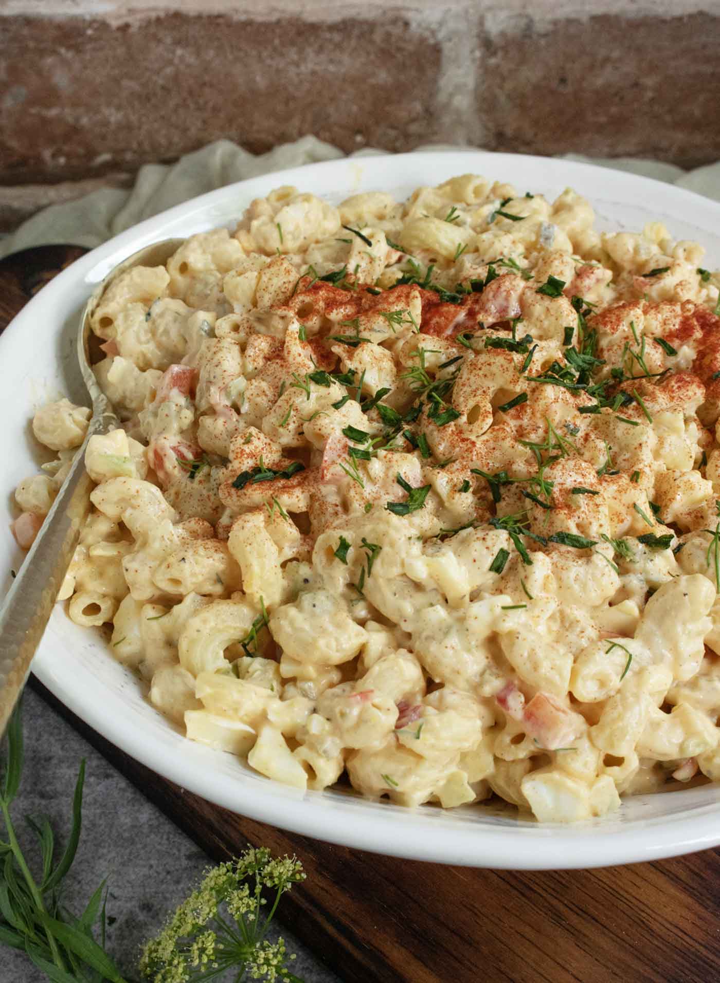Side-angled view of a white serving bowl with Deviled Egg Macaroni Salad and a serving spoon.