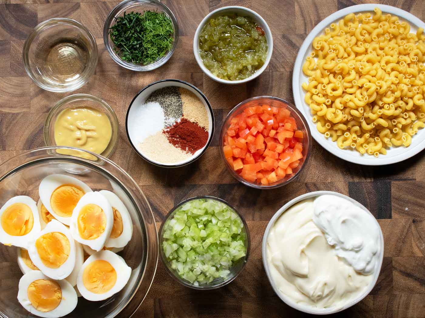 Ingredients for the macaroni salad measured out and arranged on a wooden serving board.