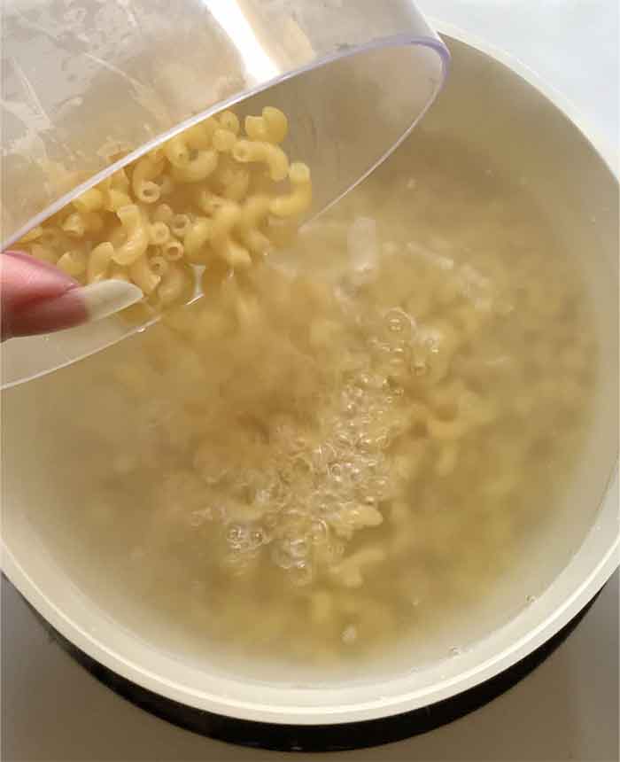 Pouring the elbow pasta into boiling water.