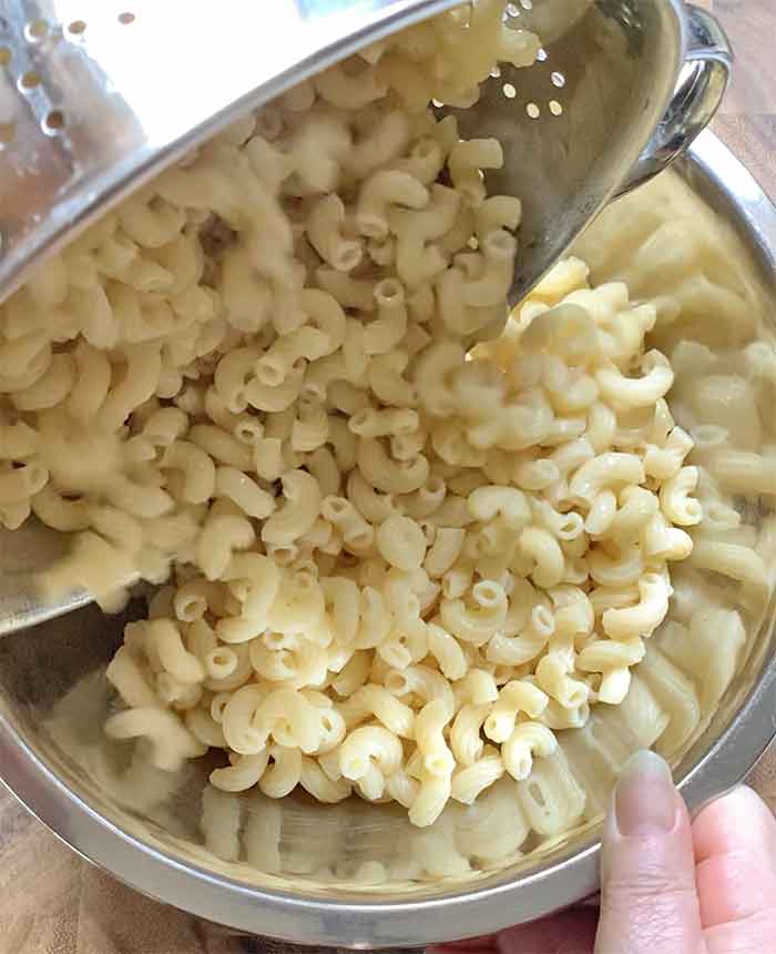 Adding the cooked, rinsed and drained pasta to a large stainless steel mixing bowl.