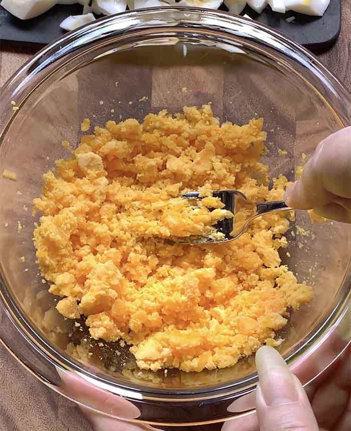 Smashing the egg yolks with a fork in a glass mixing bowl.