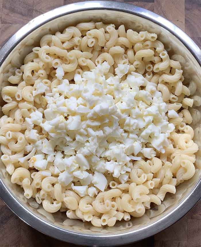 Adding chopped egg whites to the pasta in the mixing bowl.