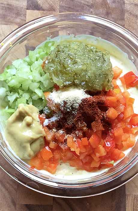Adding the remaining dressing ingredients to the mayo mixture, including pickle relish, bell peppers, mustard, celery, and spices.