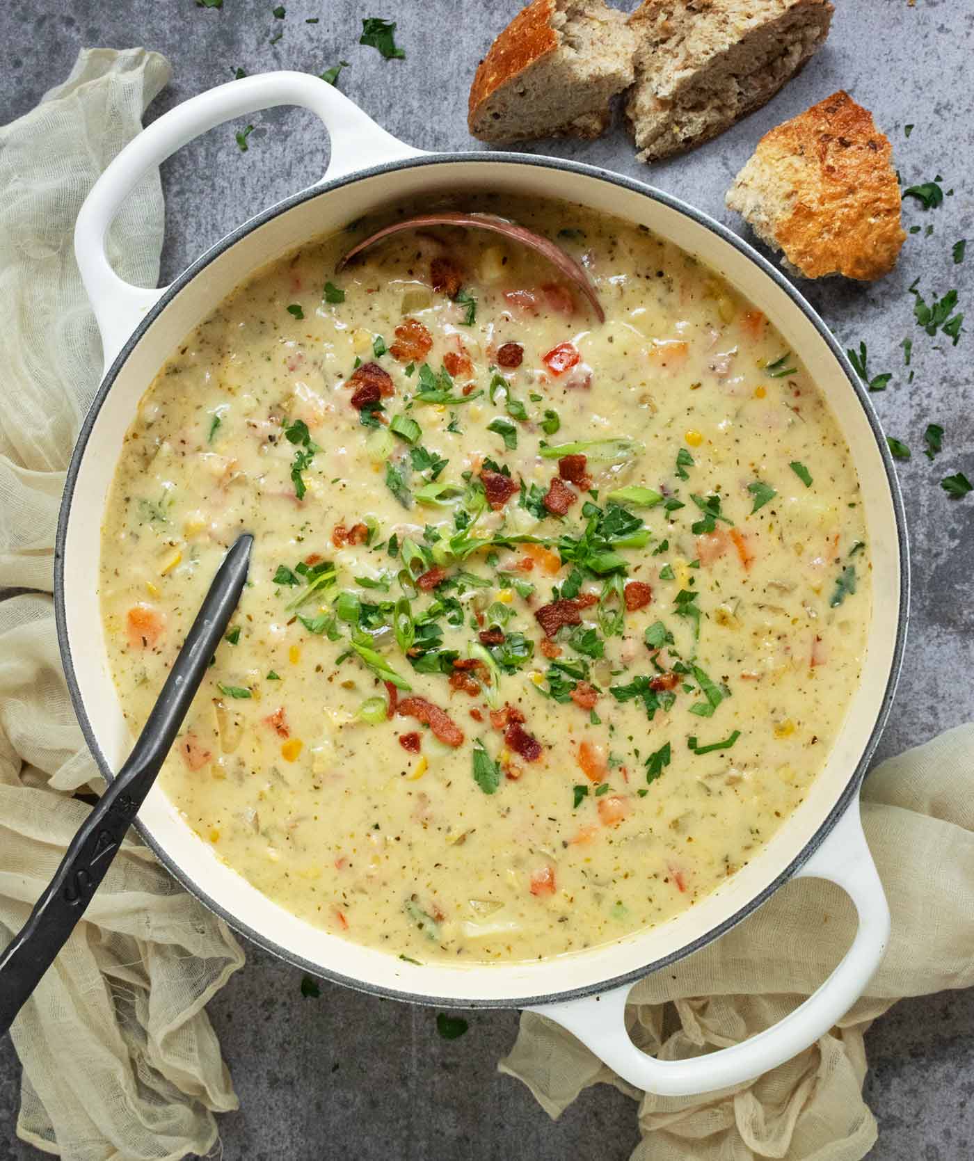 Overhead view of Ham and Corn Chowder in a large white Dutch oven, with a copper ladle.