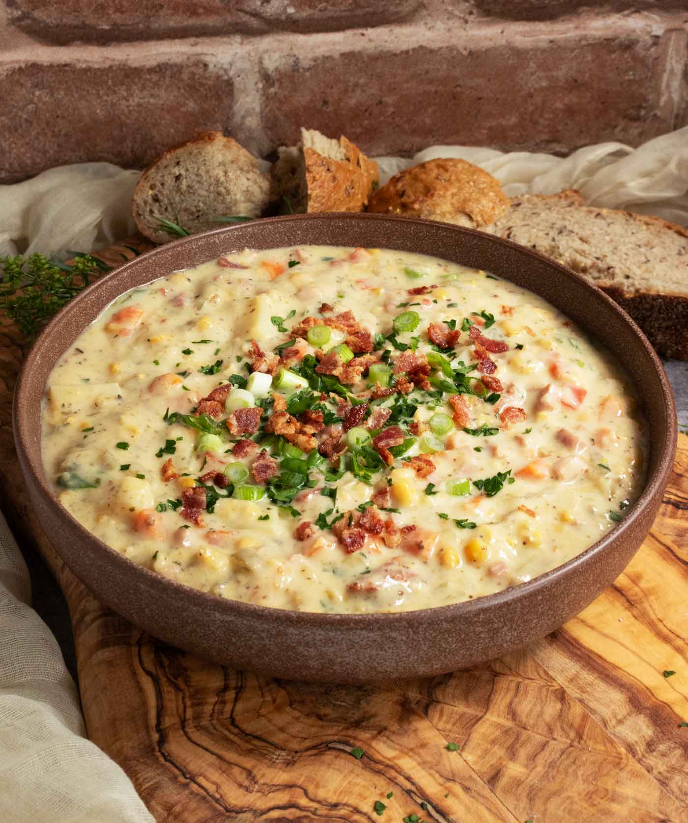 Side-angled view of Ham and Corn Chowder with chunks of fresh bread on the side.