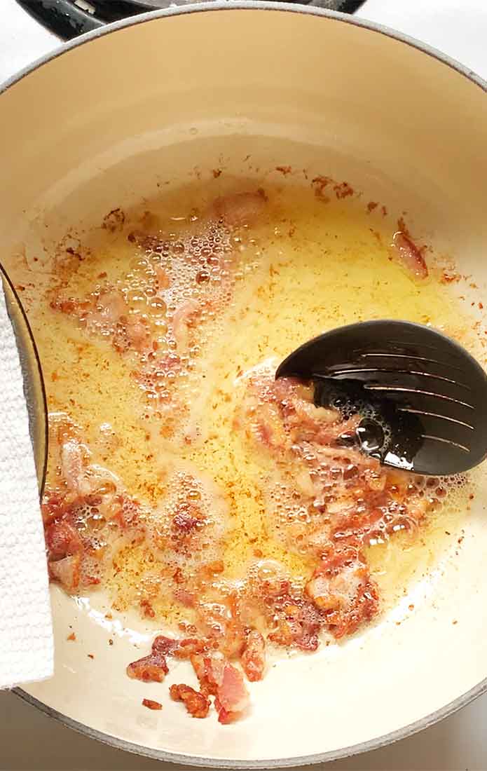 Transferring the cooked bacon to a plate using a slotted spoon.