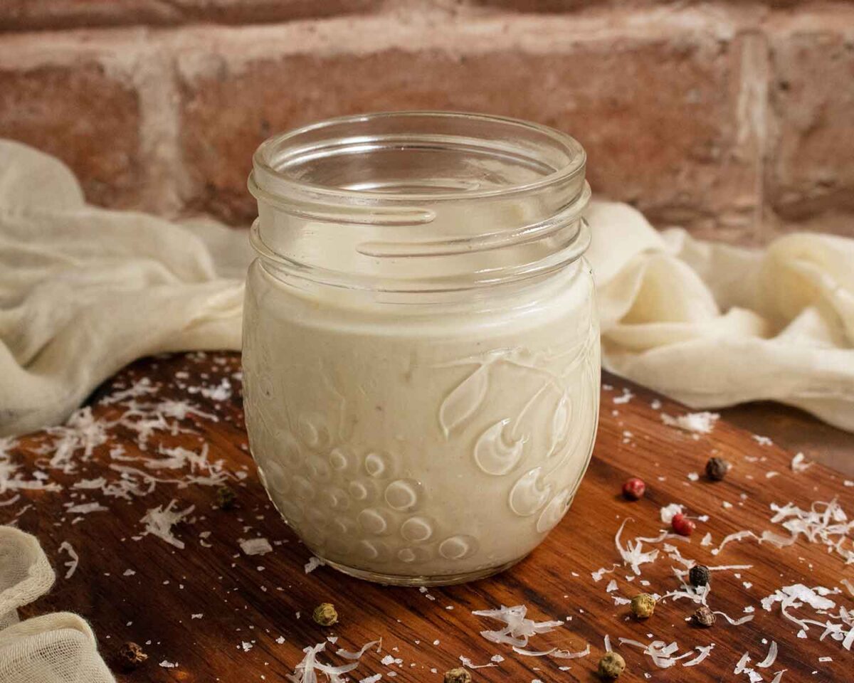 Side view of a glass jar of Caesar dressing.