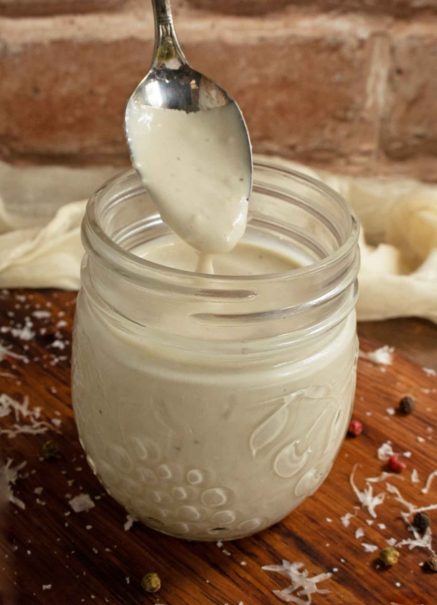 A spoonful of Caesar dressing dripping into a small glass jar.
