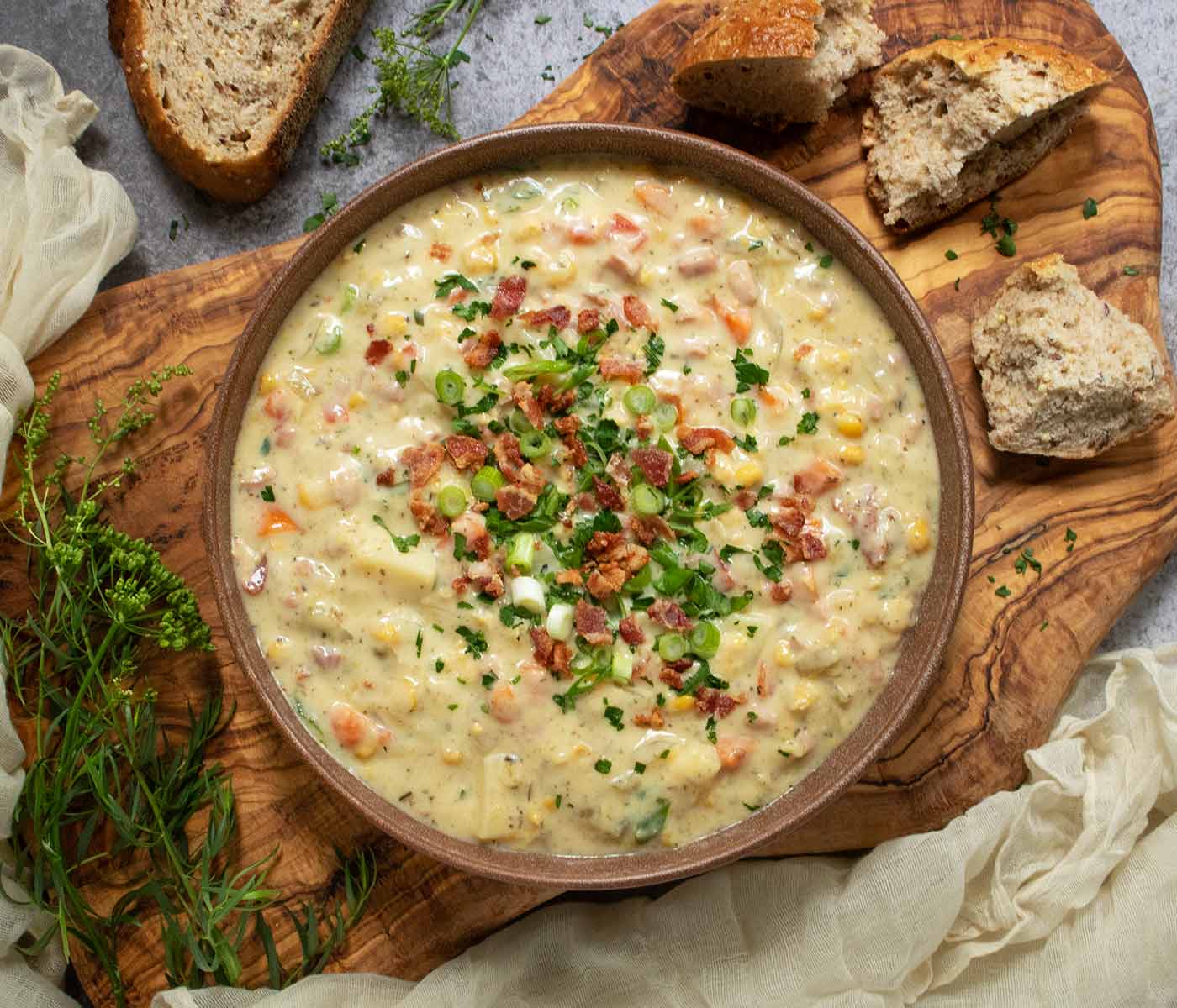 An overhead view of Ham and Corn Chowder in a brick red bowl on a wooden board.