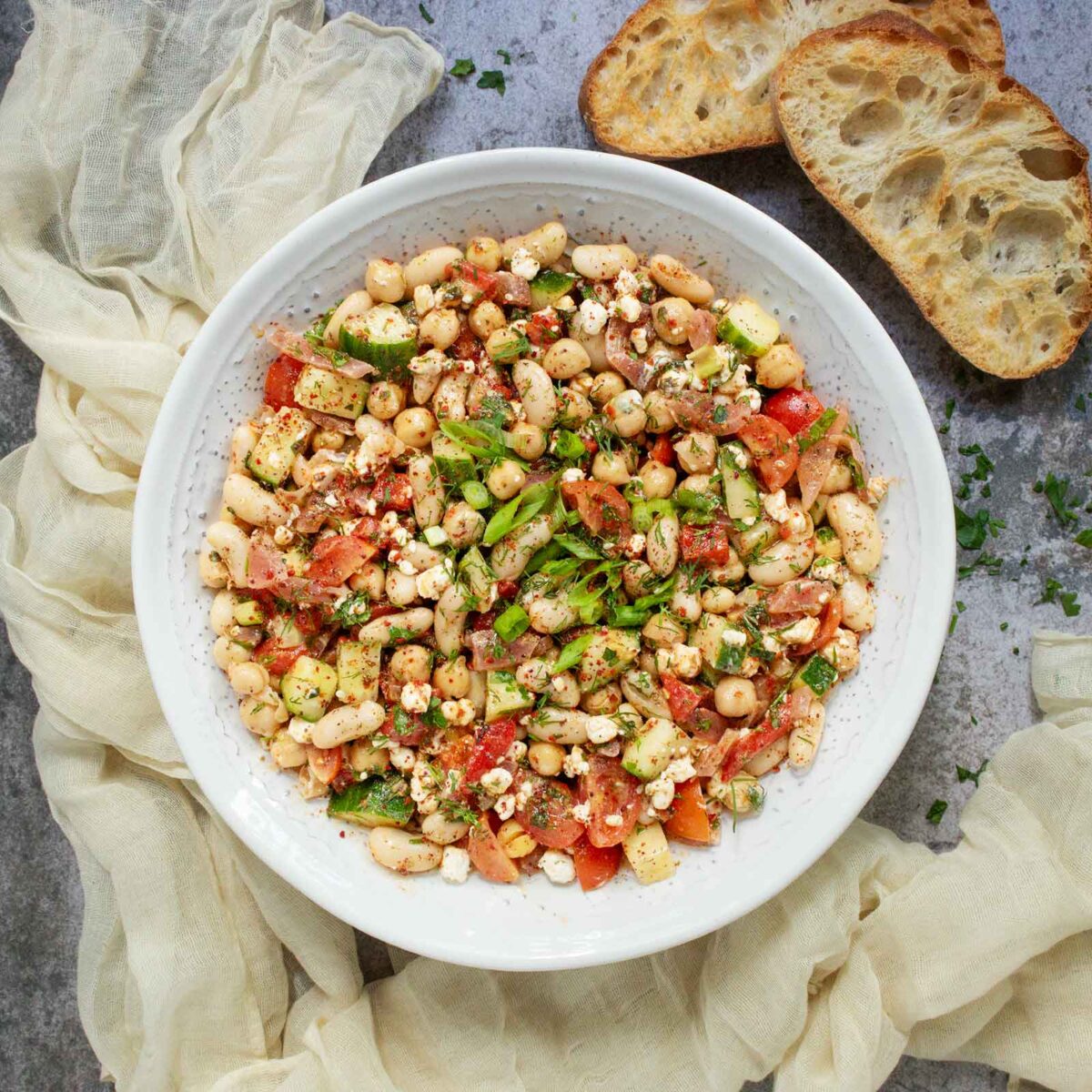 Overhead view of Mediterranean Bean Salad in a white serving bowl, with slices of toasty bread on the side.