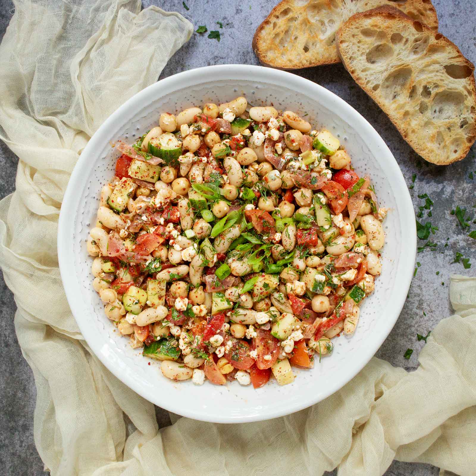 Overhead view of Mediterranean Bean Salad in a white serving bowl, with slices of toasty bread on the side.