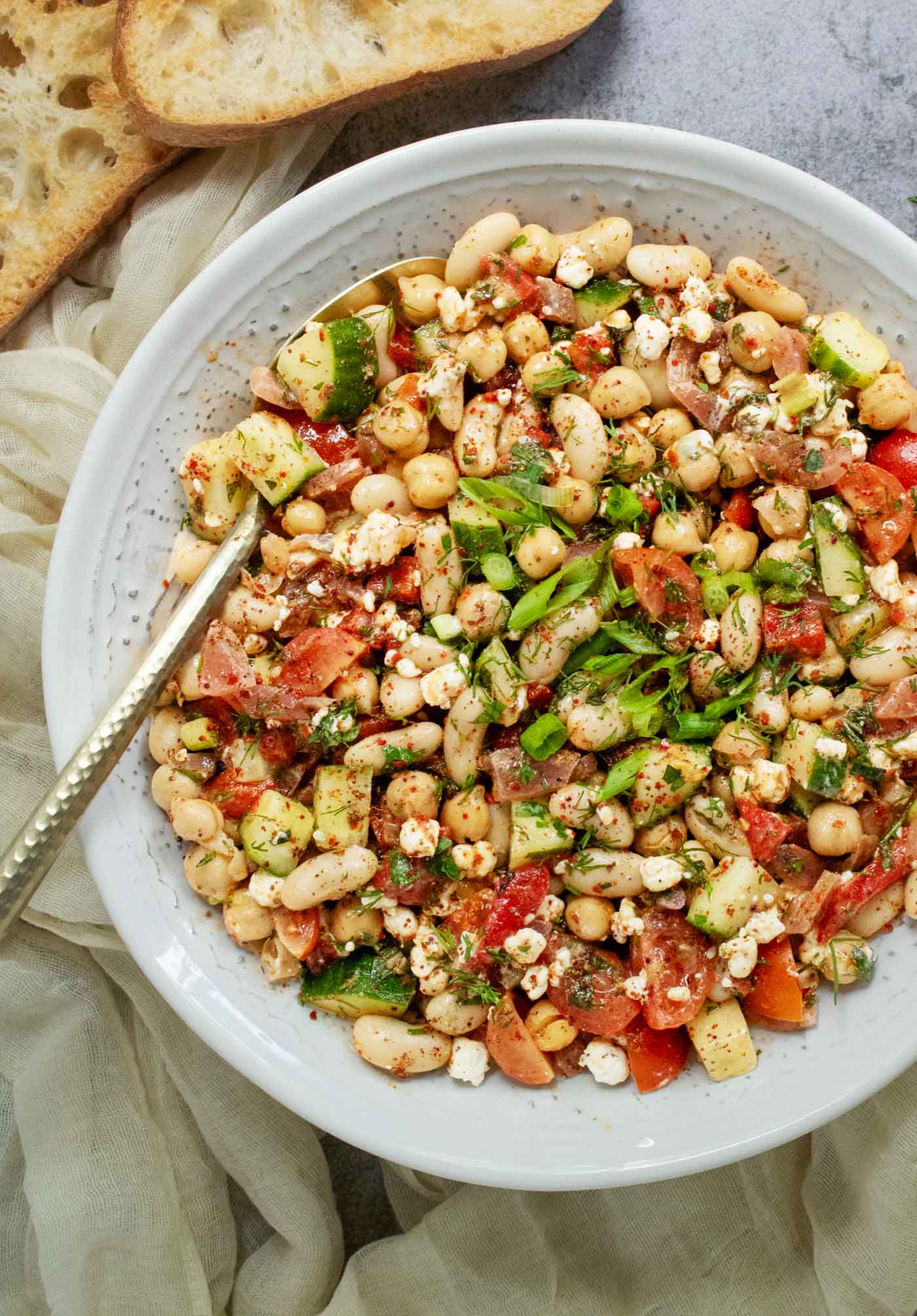 Close-up view of a bowl of Mediterrean Bean Salad with a gold-toned serving spoon.