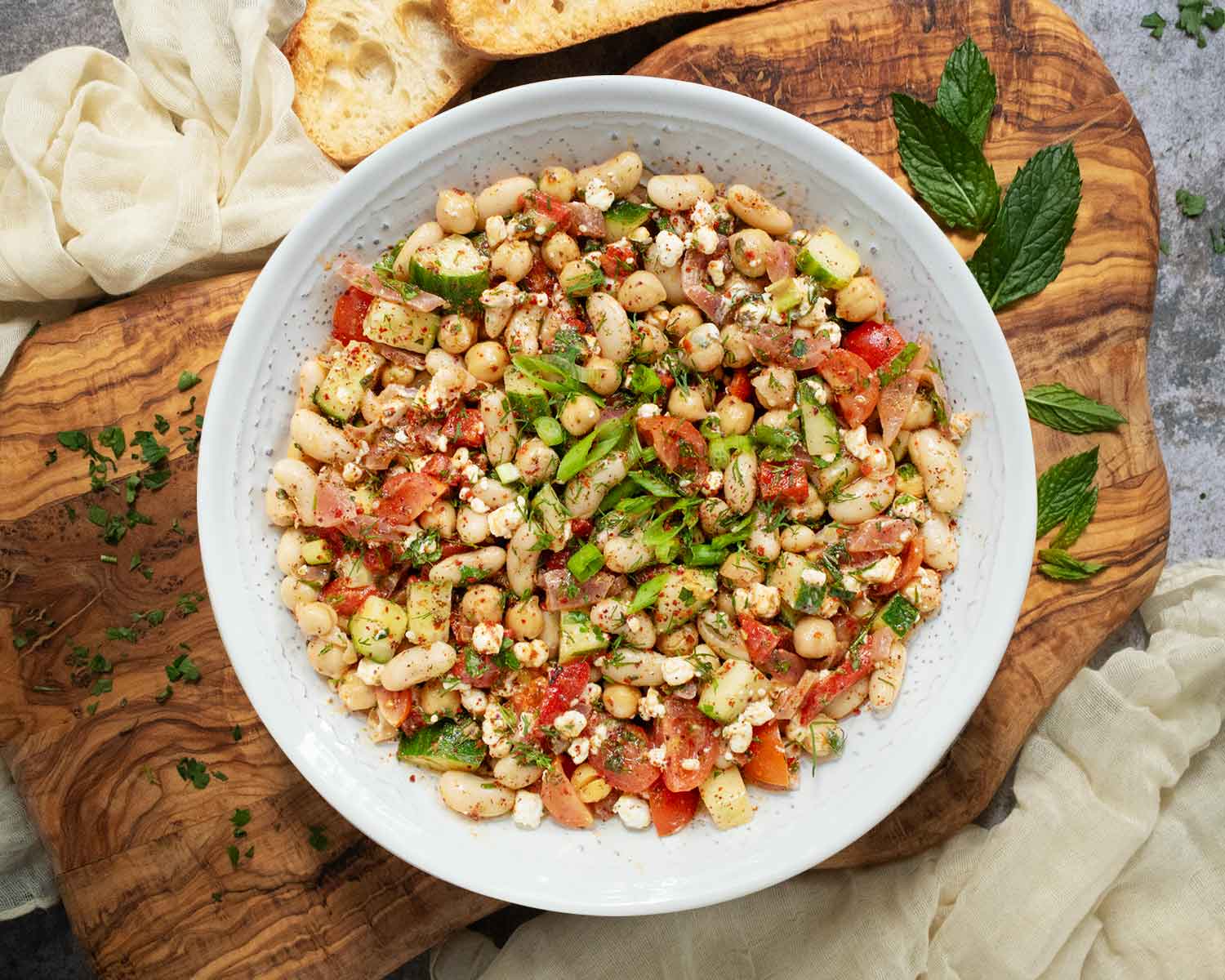 Overhead view of Mediterranean Bean Salad in a white serving bowl arranged on a wooden board.
