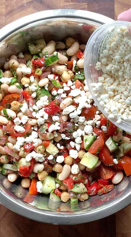 Sprinkling crumbled cheese over the top of the mixed salad.