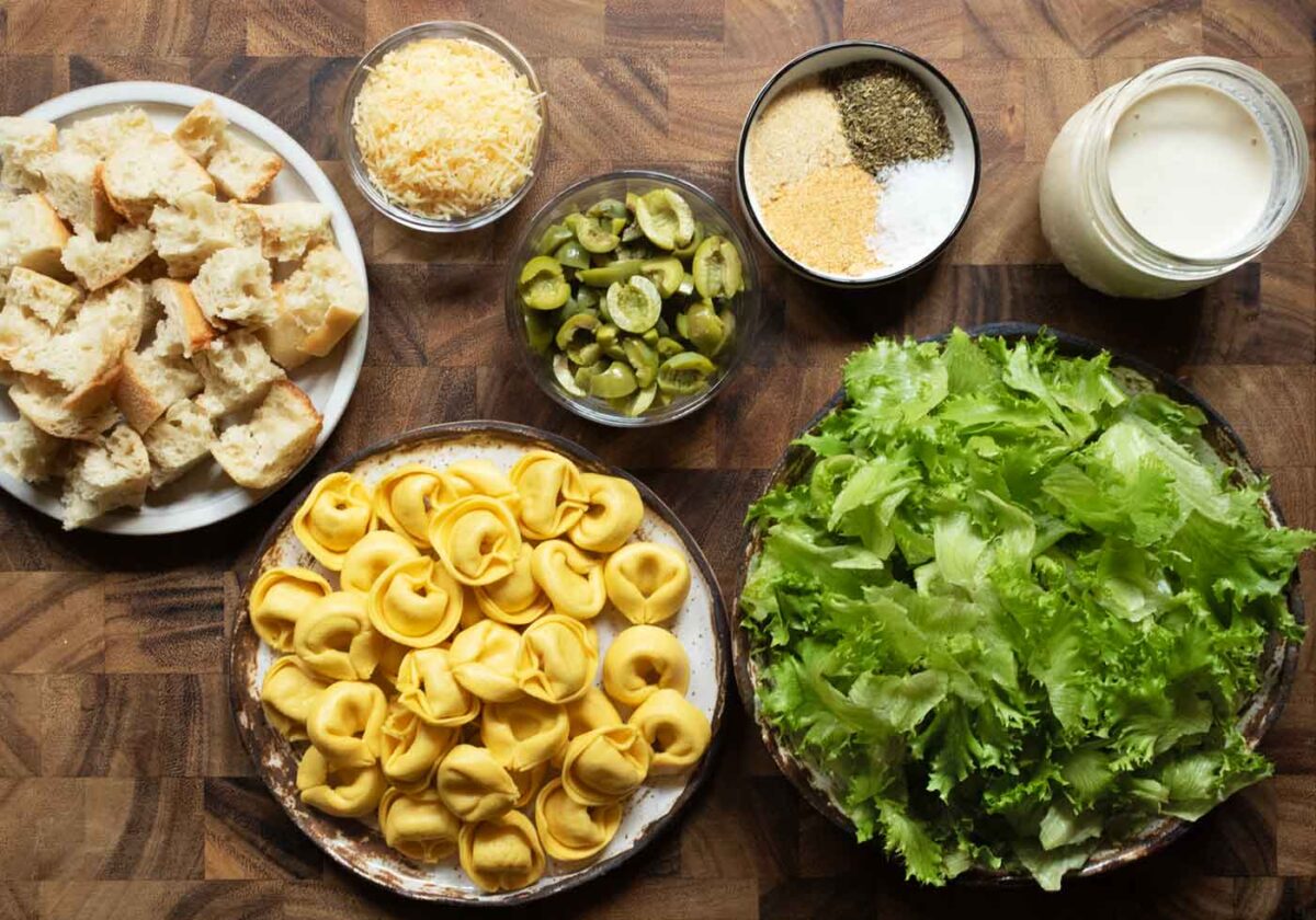 Ingredients for my Tortellini Caesar Salad prepped and arranged in bowls on a wooden board.