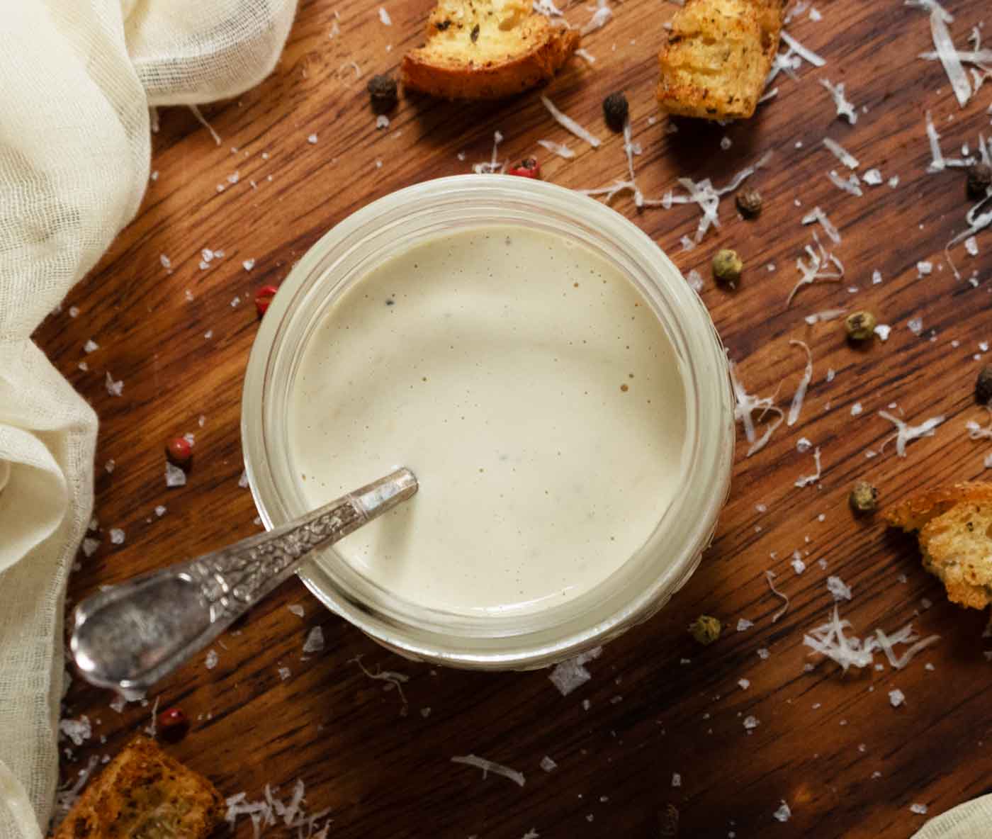 View from overhead of a glass jar filled with Easy Caesar Dressing, with a spoon sitting in the jar.