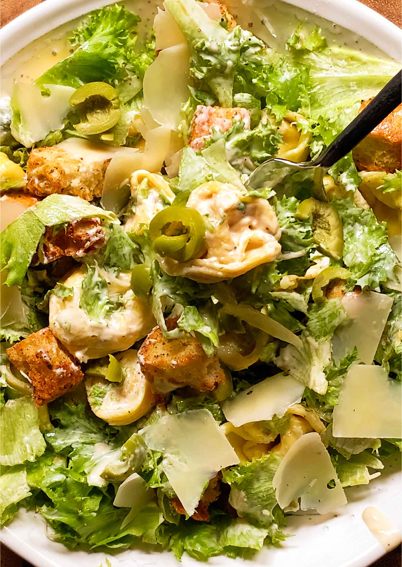 A close-up view of a bowl of Tortellini Caesar Salad with a fork digging into the salad.