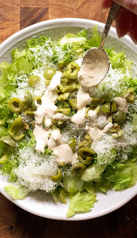 Drizzling Caesar dressing over lettuce, olives, and parm.
