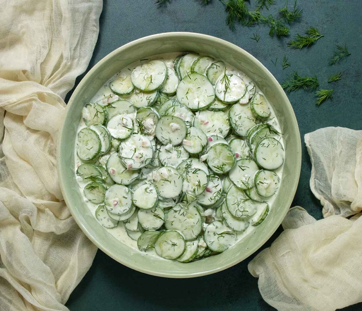 Overhead view of Creamy Tzatziki Cucumber Salad in a light green bowl against a dark green background.