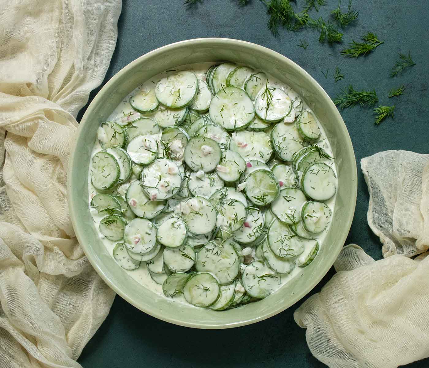 Overhead view of Creamy Tzatziki Cucumber Salad in a light green bowl against a dark green background.