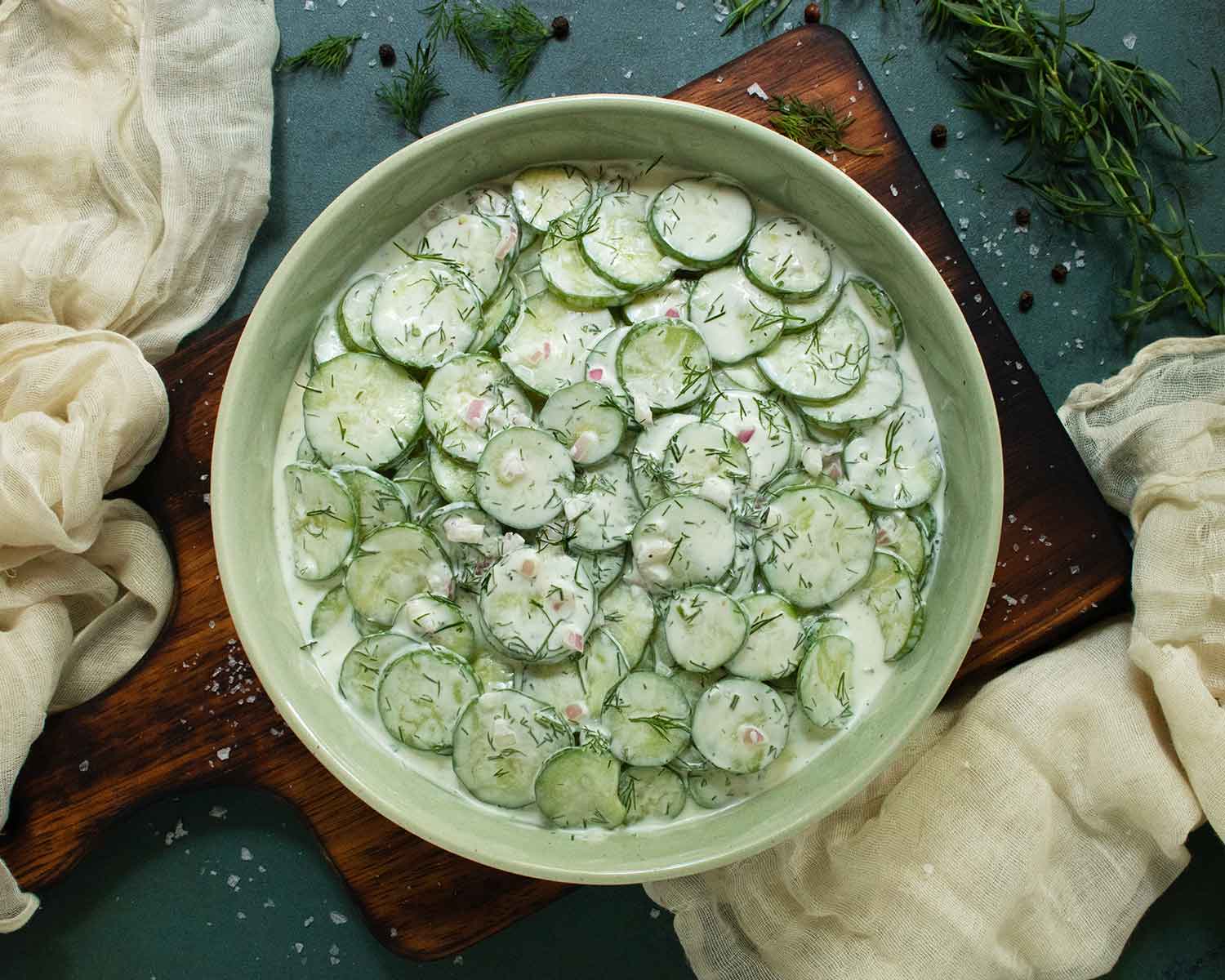Overhead view of Creamy Tzatziki Cucumber Salad in a light green bowl on a dark wooden serving board.