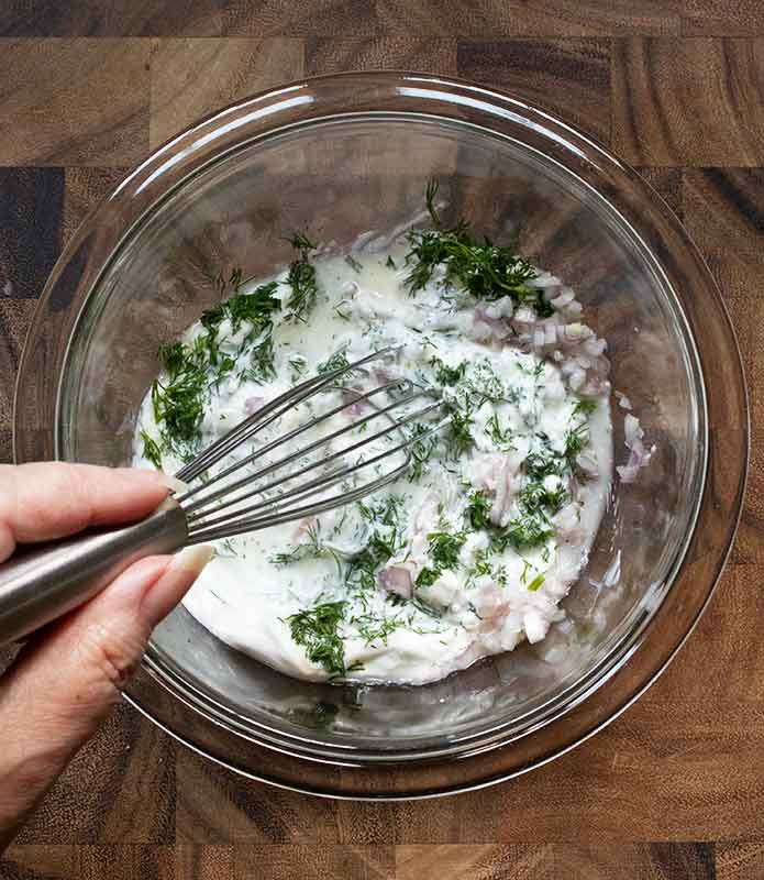 Whisking the dressing ingredients together in a glass bowl.