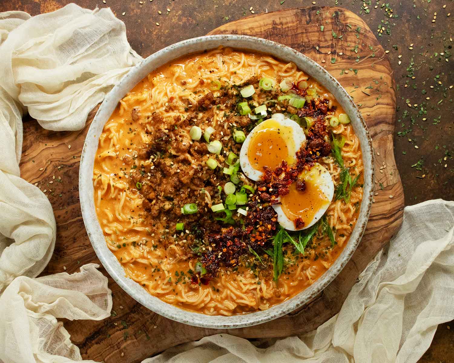 Overhead view of Spicy Peanut Chili Crisp Ramen Noodle Soup in a rustic bowl on a wooden board.